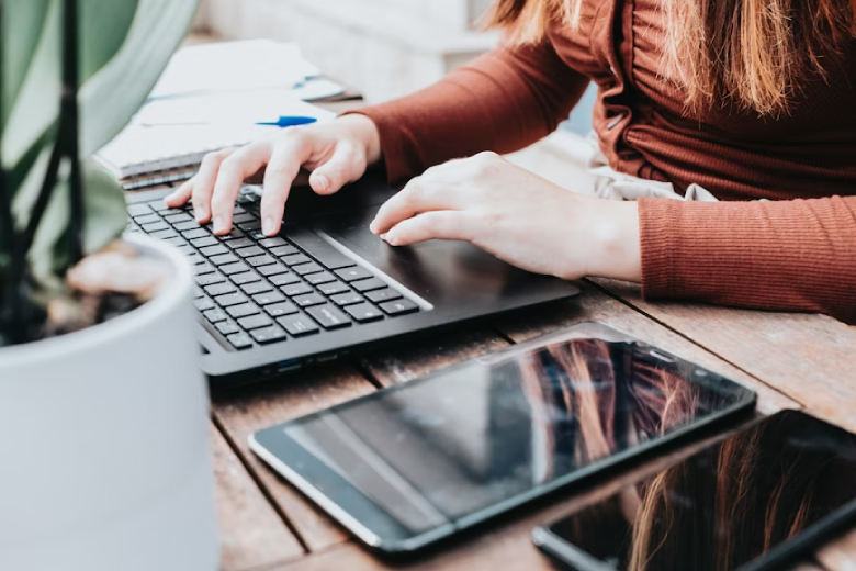 Mulher usando um notebook com um celular e um tablet ao lado