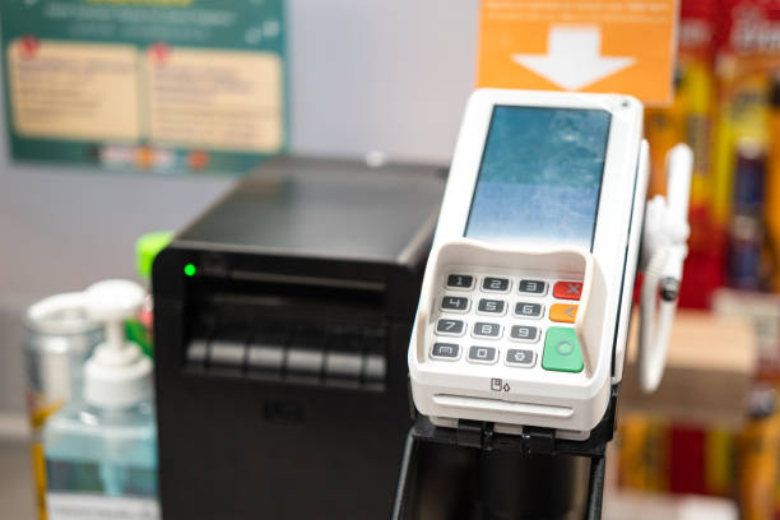 Imagem mostrando uma maquininha de pagamento em destaque num estabelecimento comercial