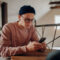 Jovem de visual casual e óculos usando smartphone em um ambiente interno moderno.